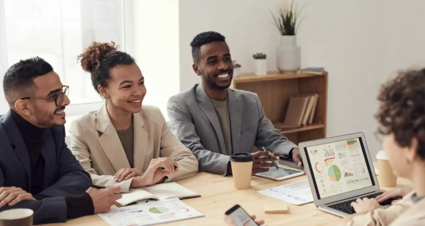 Four people smiling and talking at a work meeting.